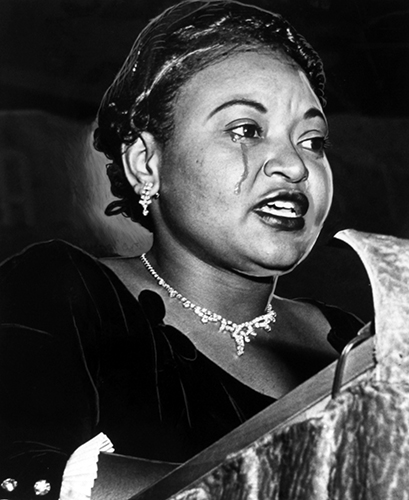 Mamie Till cries while speaking at a podium. She is wearing a black dress.