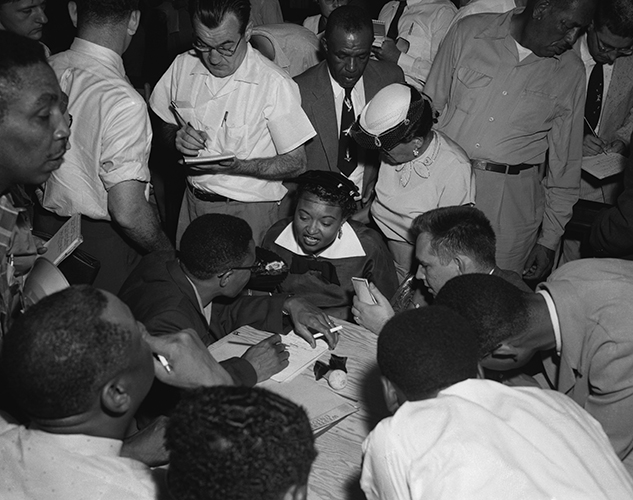 Black and white photo of Mamie Till, mother of Emmett Till, sitting surrounded by members of the press.