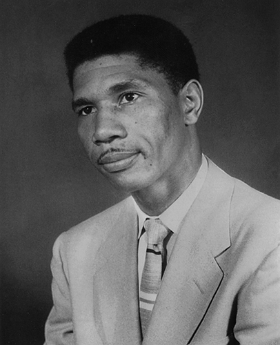 A black and white photo of Medgar Evers wearing a grey suit and tie.